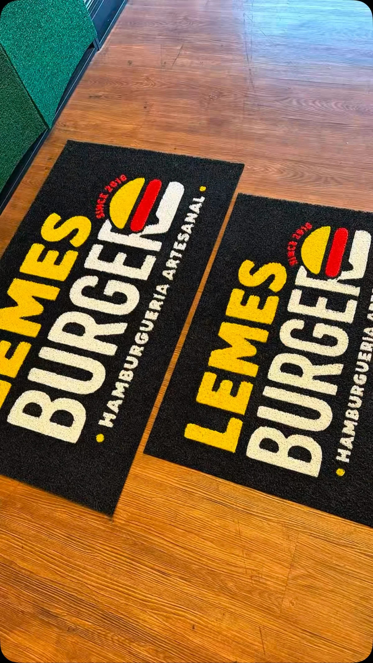 Tapetes da Lemes Burger com logotipo amarelo e vermelho sobre fundo preto