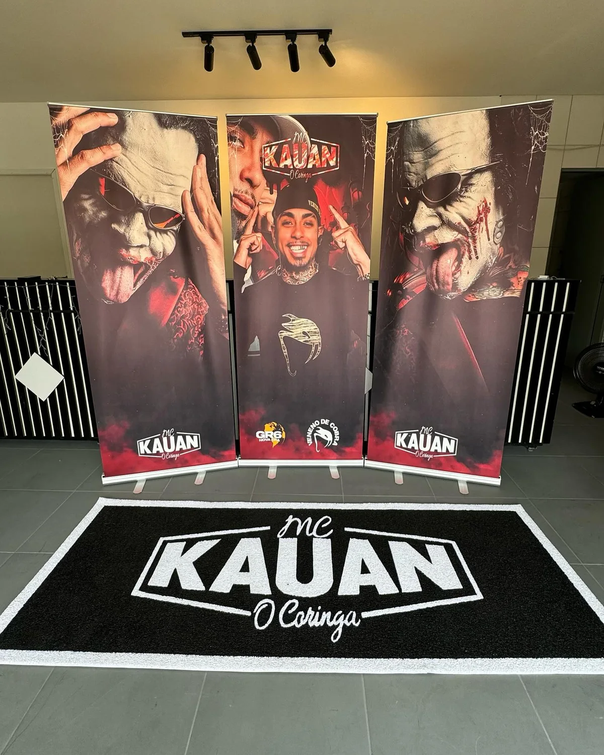 Tapete preto e branco MC Kauan O Coringa, em frente a três banners do artista