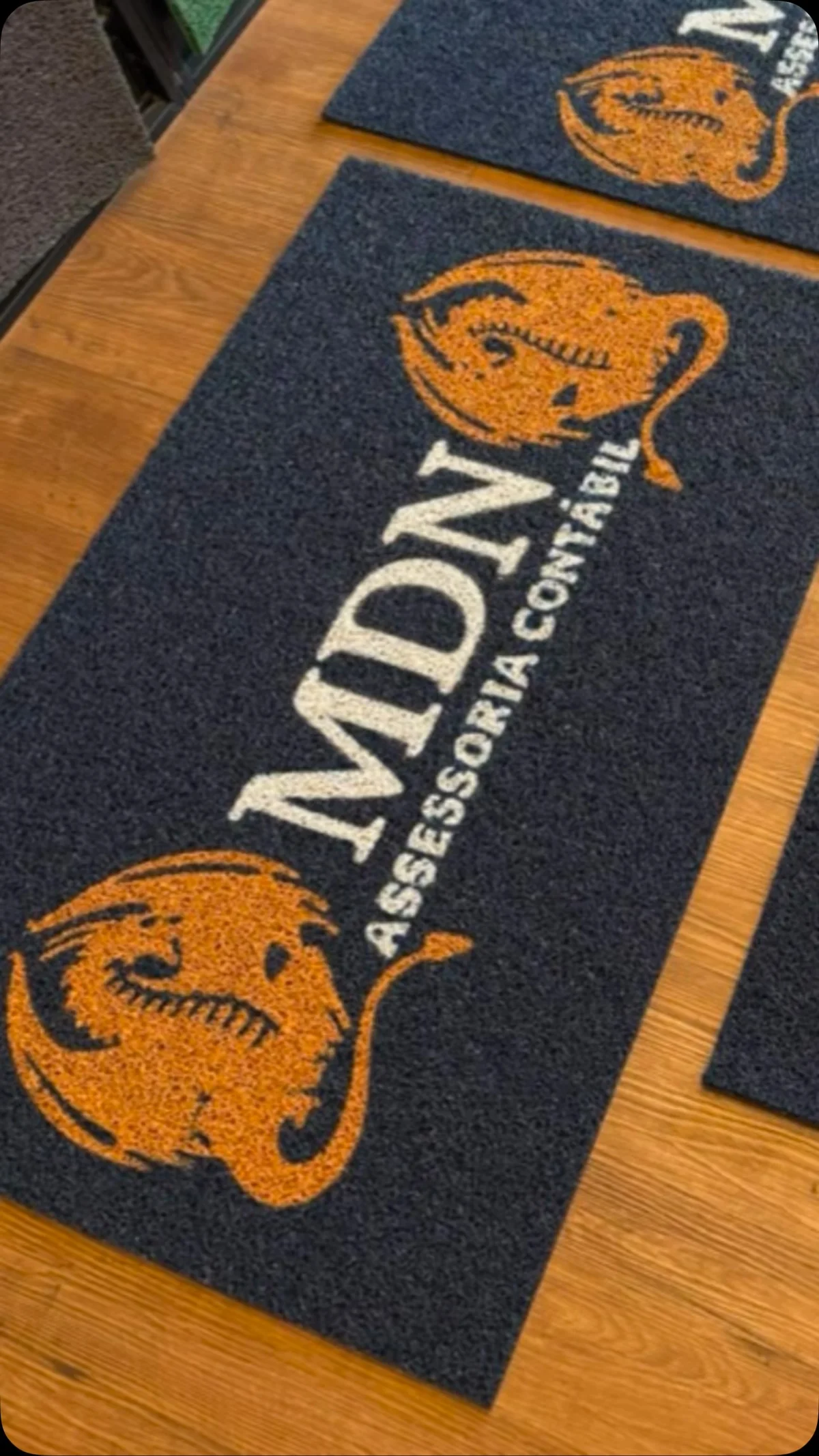 Dois tapetes azul-escuros da MDN Assessoria Contábil, com texto branco e símbolo dourado